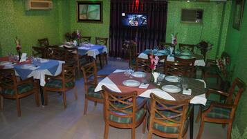 A restaurant with multiple tables and chairs, green walls, and a television screen.