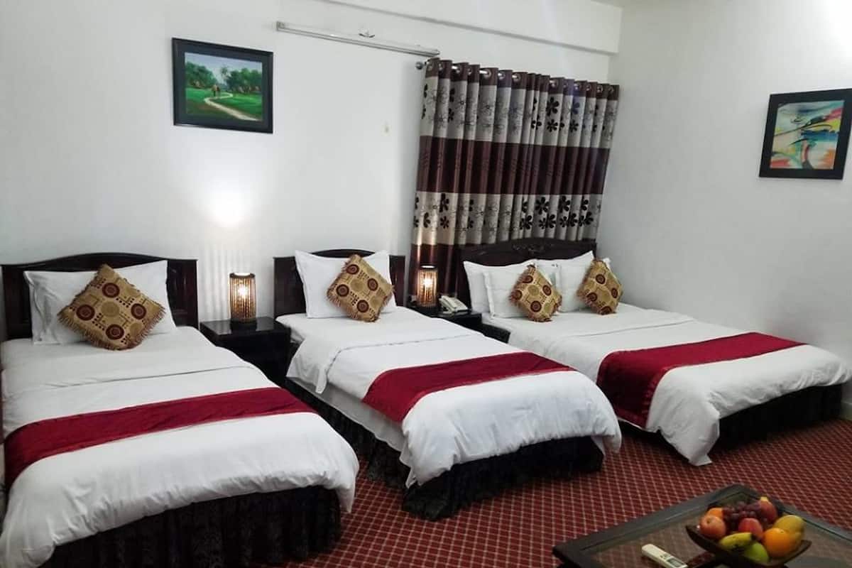 A hotel room with three beds, each with white bedding and patterned pillows. There is a small table with fruit and a thermometer.