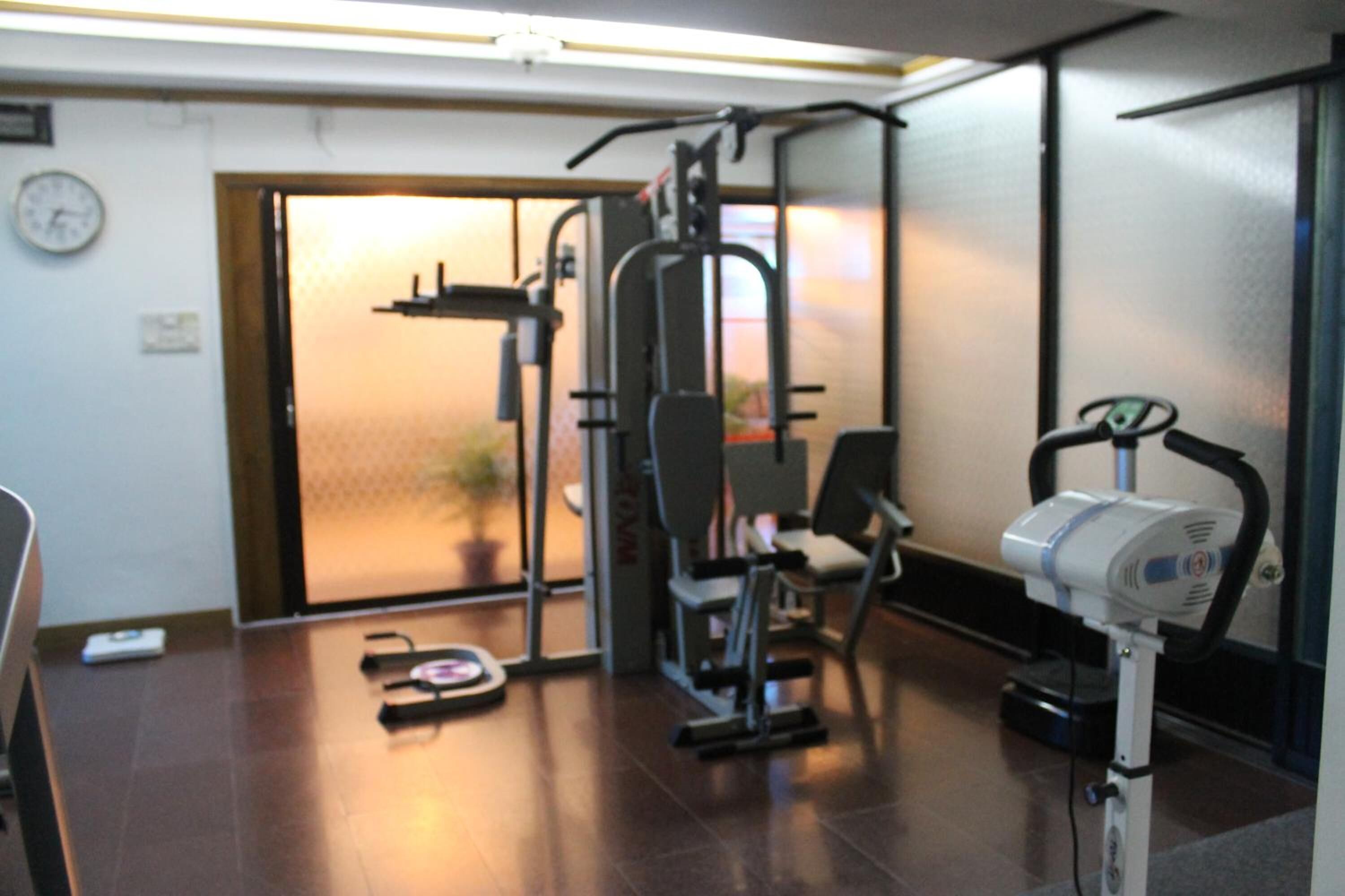 Een sportschool met fitnessapparatuur, een weegschaal en een klok aan de muur.