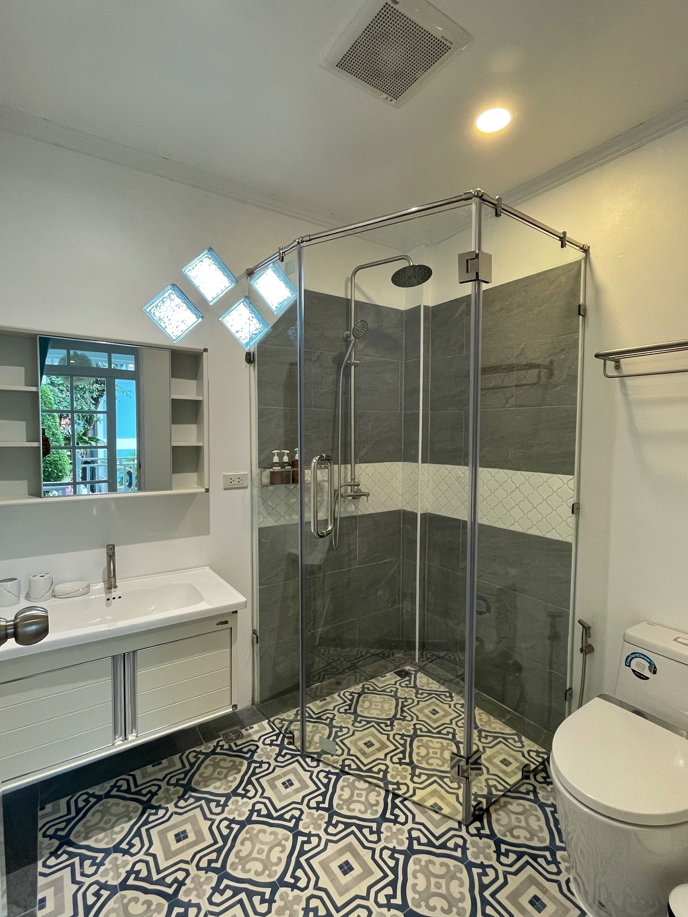 Un baño moderno con ducha de vidrio, lavabo blanco y piso estampado.
