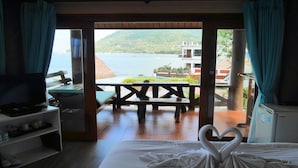 Ein Hotelzimmer mit Bett, Fernseher, Schreibtisch und Blick auf ein Gewässer sowie ein Gebäude am anderen Ufer.