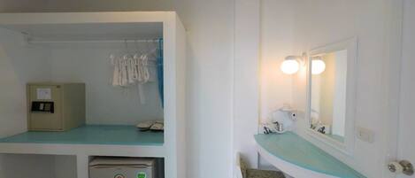 A compact room with a kitchenette, a small refrigerator, a sink with a mirror, and a chair.