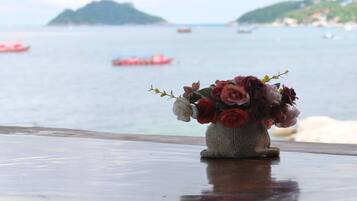 Un vase de fleurs est posé sur une table en bois, avec une vue sur la mer et des bateaux en arrière-plan.