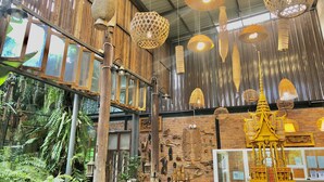 Quarto com paredes de madeira, luminárias tecidas suspensas e parede de tijolos com figuras de madeira entalhadas.