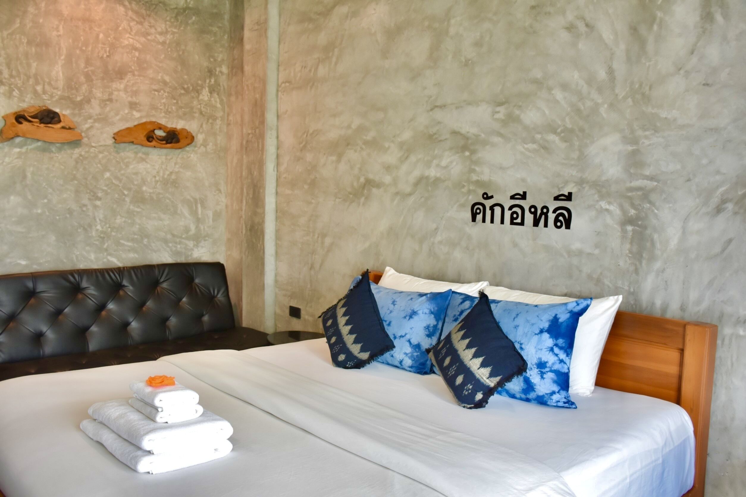 A neatly made bed with white linens and blue patterned pillows, a tufted headboard, and a wall with a textured surface and two wooden objects.