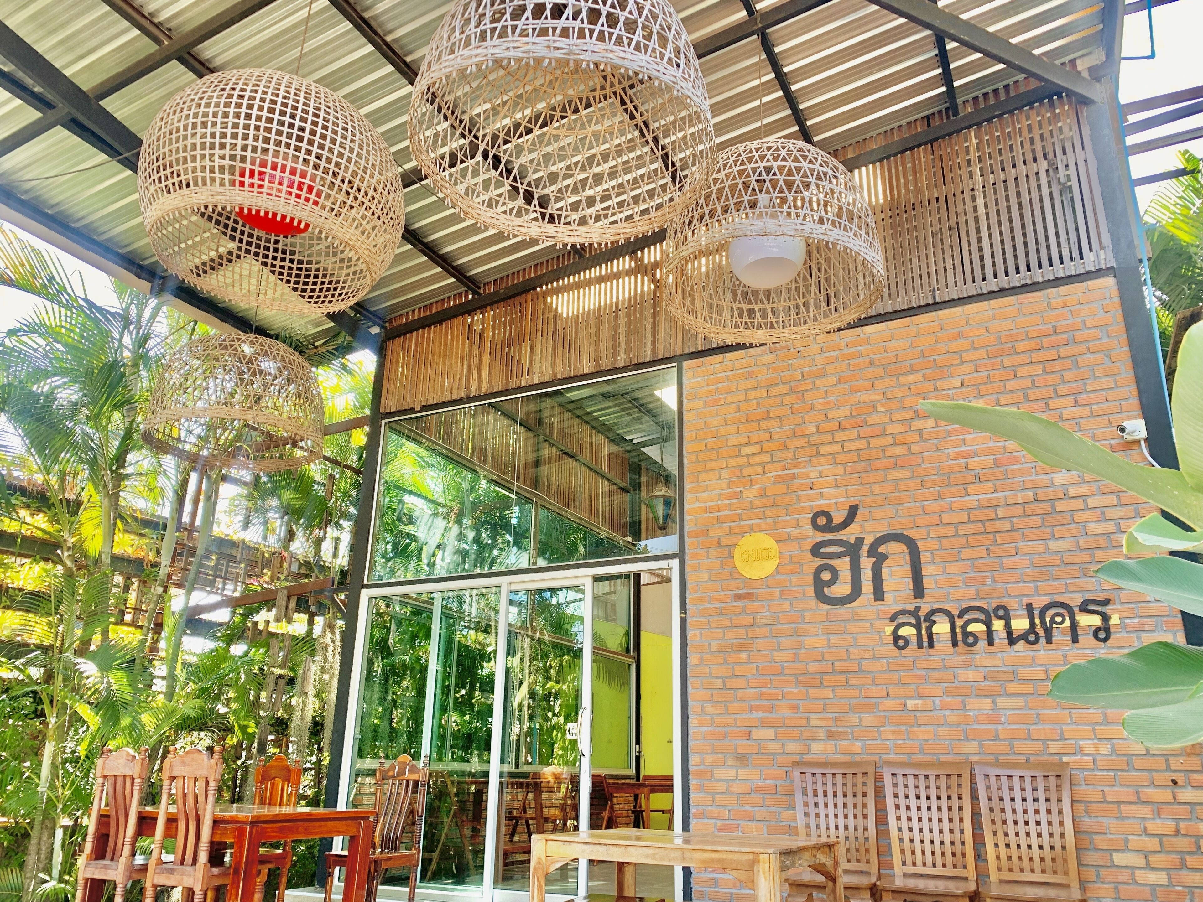 Un restaurante con lámparas colgantes de mimbre, muebles de madera y una pared de ladrillo con escritura tailandesa.