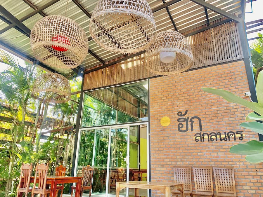 Un restaurante con lámparas colgantes de mimbre, muebles de madera y una pared de ladrillo con escritura tailandesa.