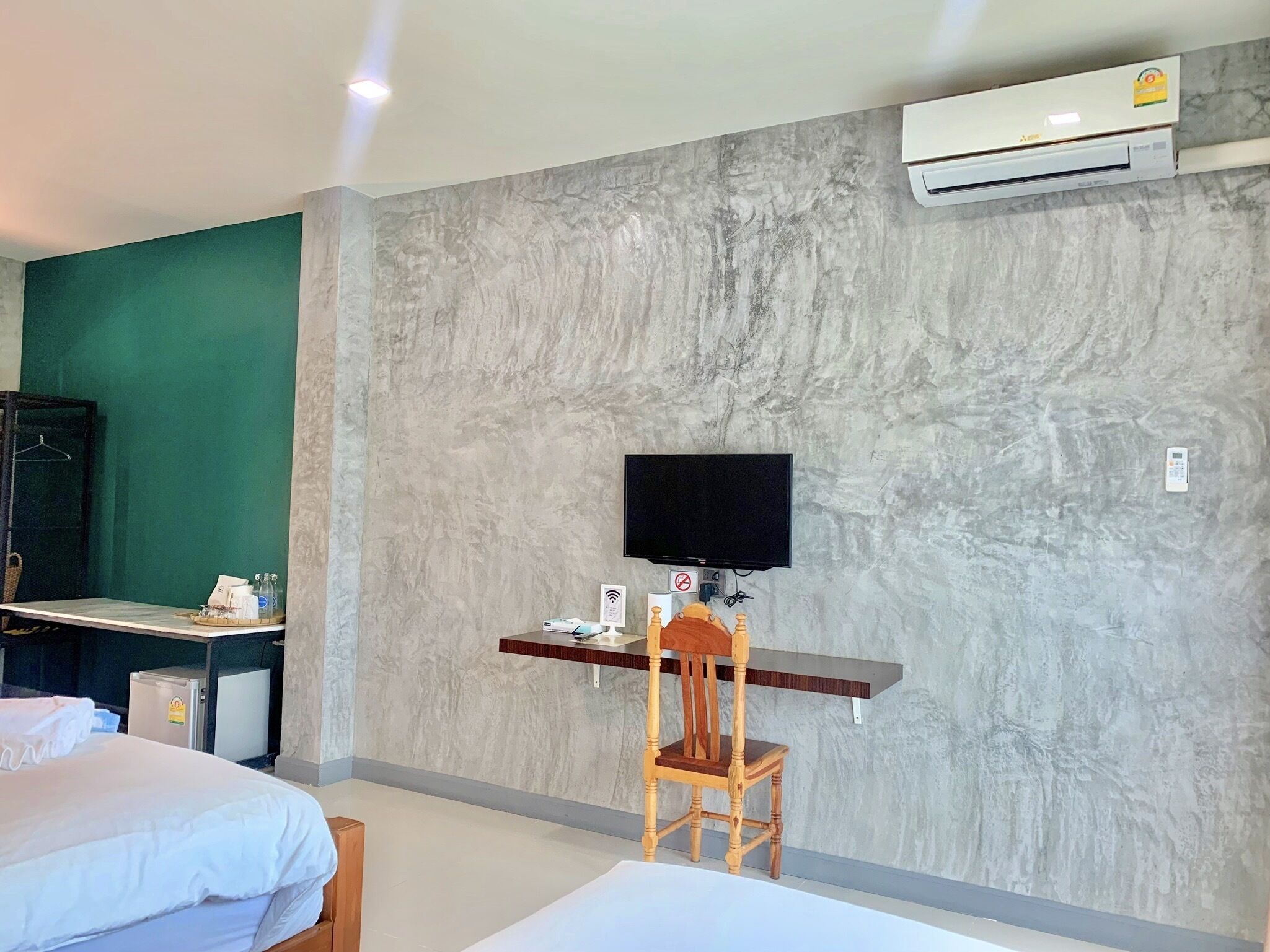 A hotel room with a bed, a desk with a computer, a chair, a television, and an air conditioning unit.