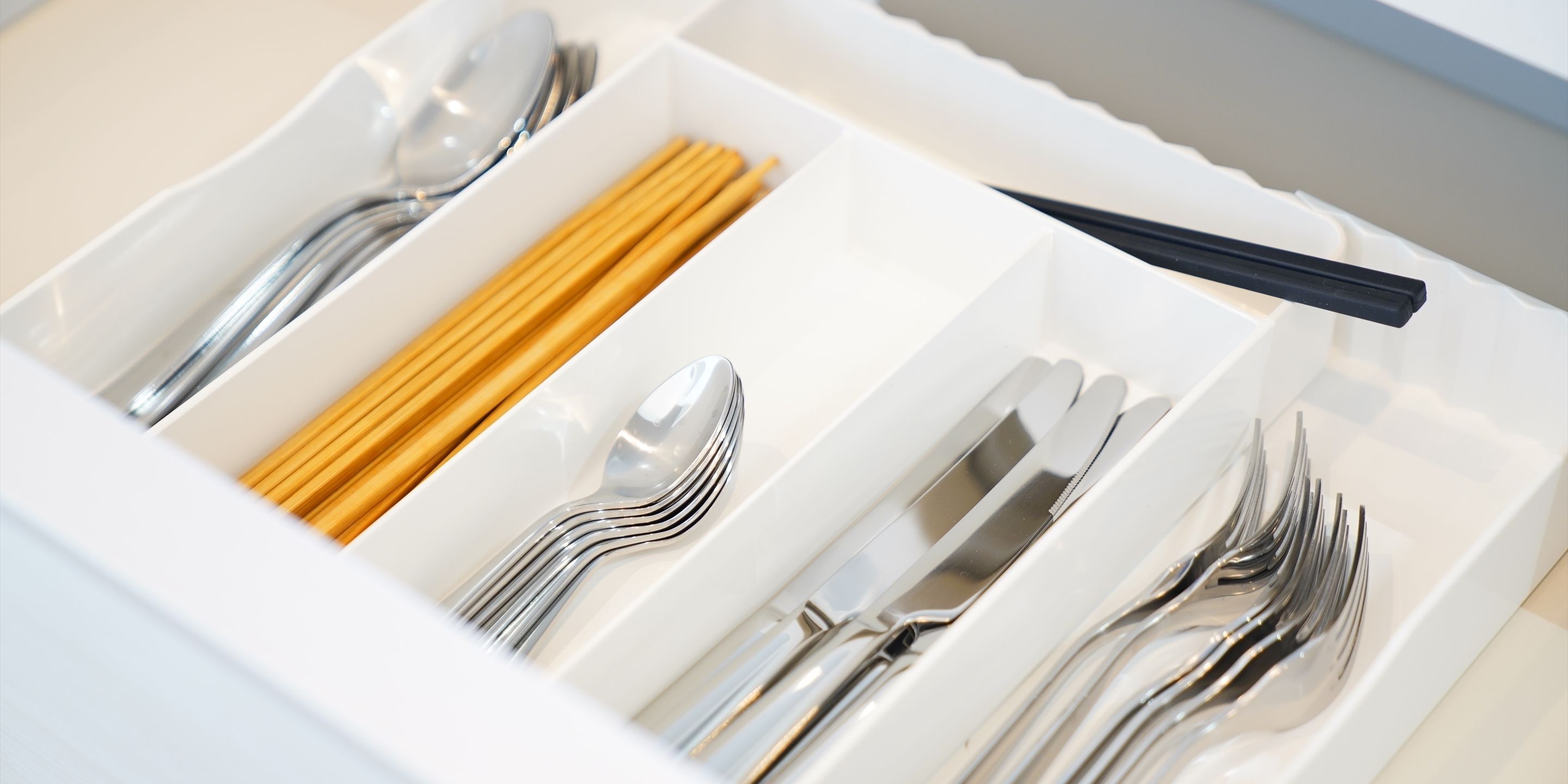 A drawer with neatly organized utensils including forks, spoons, and chopsticks.