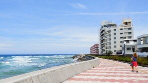 Une promenade en bord de mer offrant une vue sur l’océan, avec un immeuble à plusieurs étages en arrière-plan.