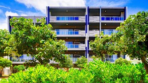 Un immeuble à plusieurs étages, doté de balcons et de grandes fenêtres, entouré d’une végétation luxuriante.