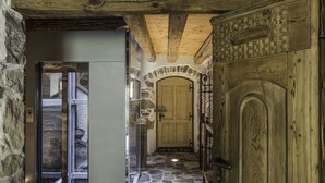 A stone-floored corridor with a wooden door and a glass door leading to a room. - Maso Franceschella (Ville di Fiemme)