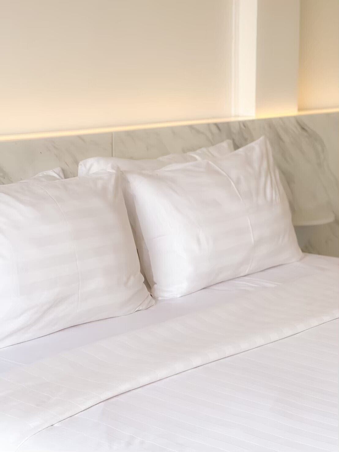 Een netjes opgemaakt bed met witte lakens en kussens, een marmeren hoofdbord en een wandlamp.