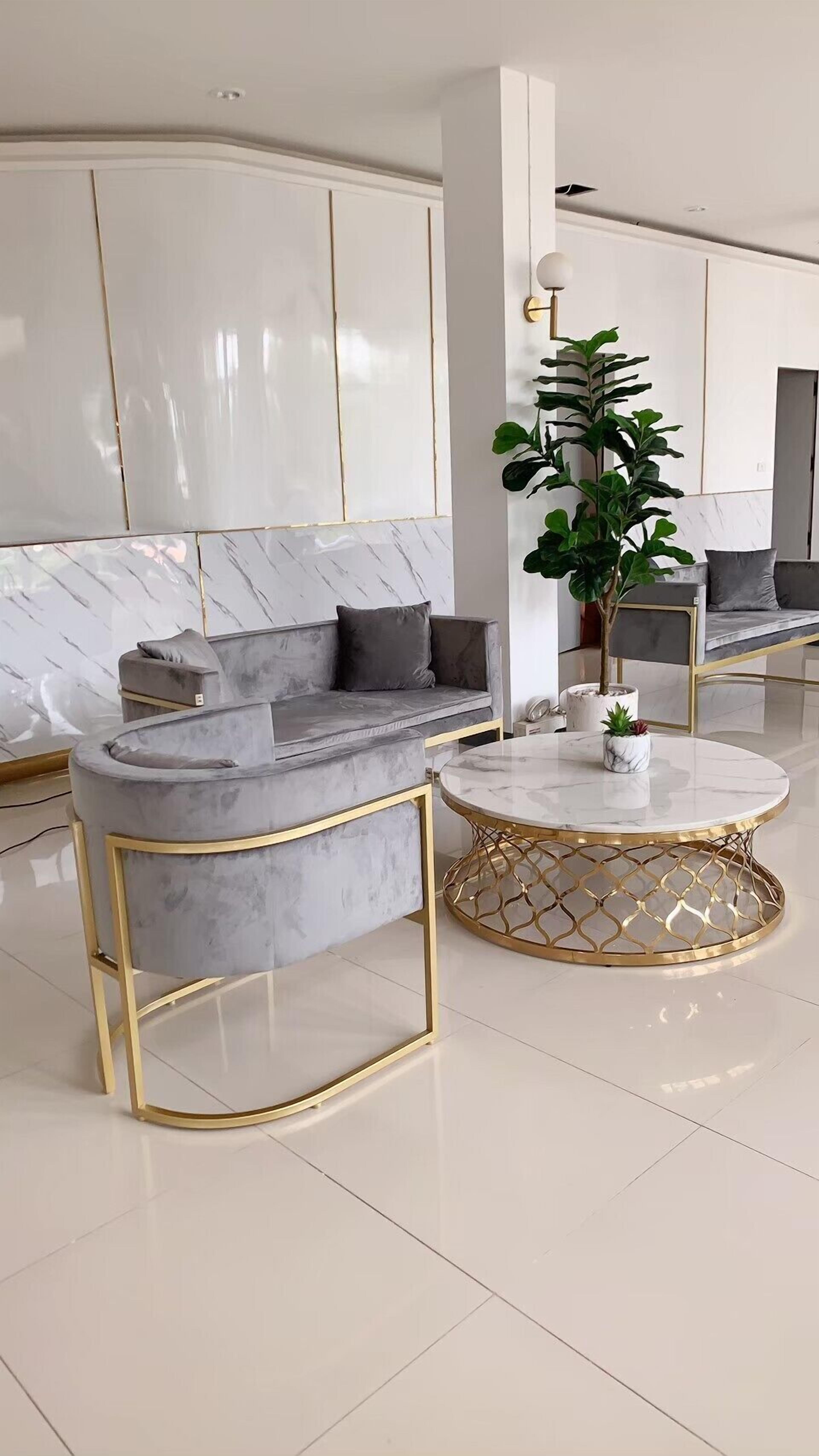 Una sala de estar moderna con un sofá gris, una mesa de centro redonda con patas doradas y una planta en maceta.
