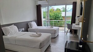 Habitación de hotel con dos camas, un escritorio y vistas al exterior a zonas verdes.