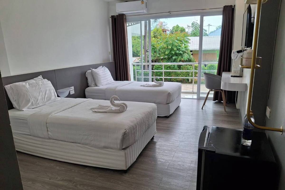 Une chambre d’hôtel avec deux lits, un bureau et une vue sur la verdure environnante.
