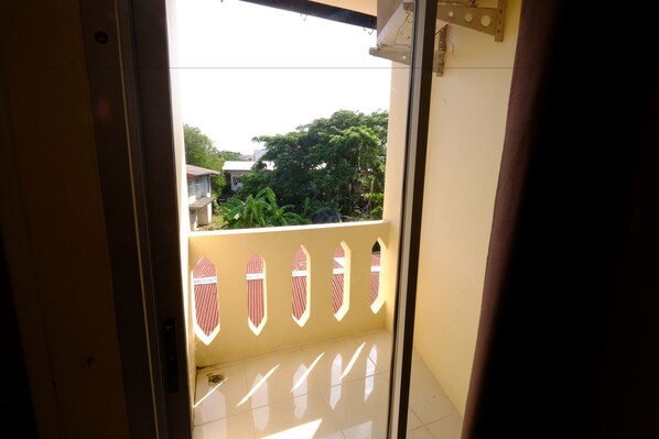 An interior view of a hotel room with a balcony featuring a decorative railing and a view of greenery outside.