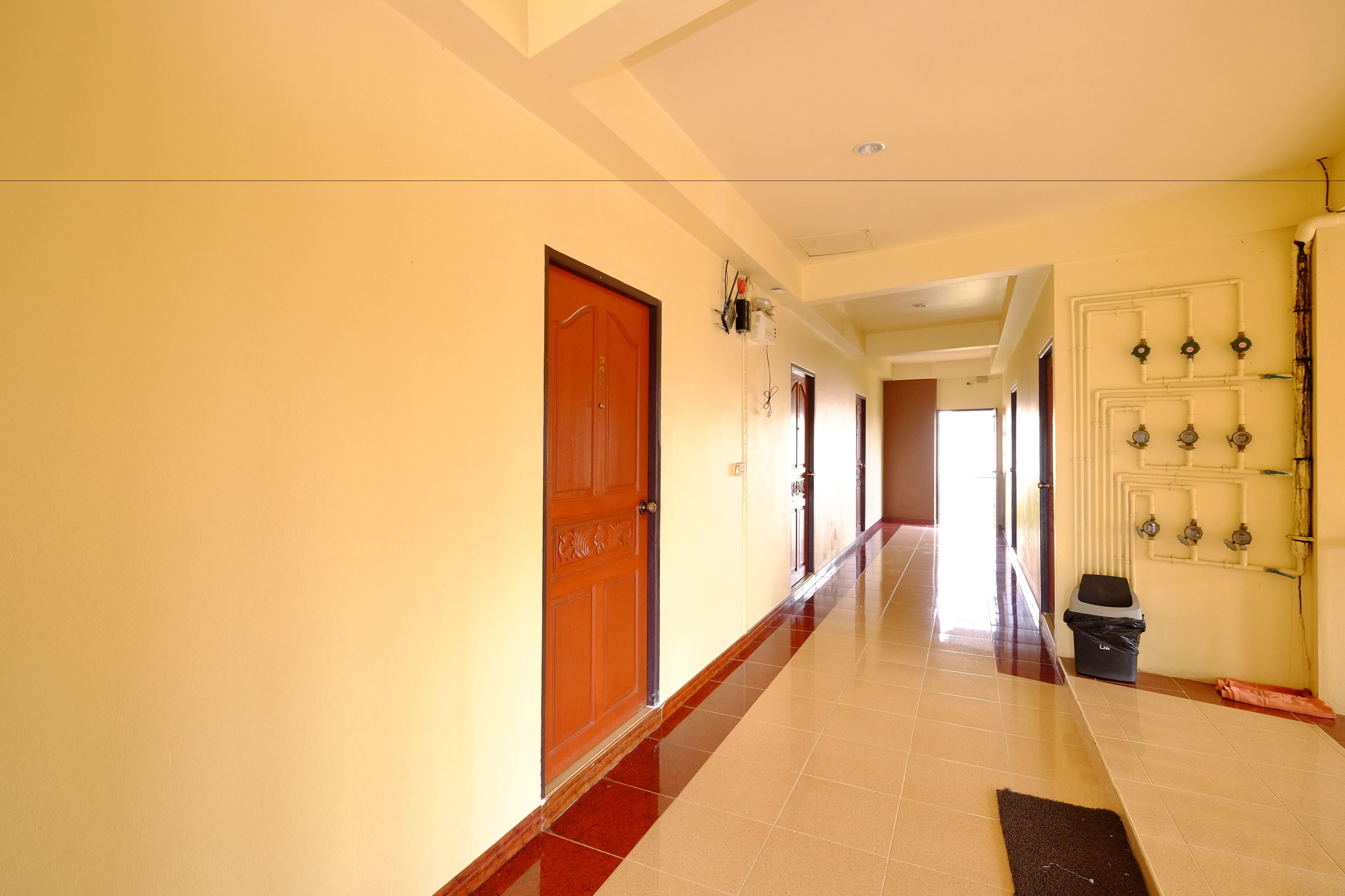 A long, narrow hallway with wooden doors on one side and a wall with multiple light fixtures on the other.