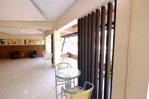A spacious lobby with a reception desk, a seating area with tables and chairs, and a view of the outside through a large window.