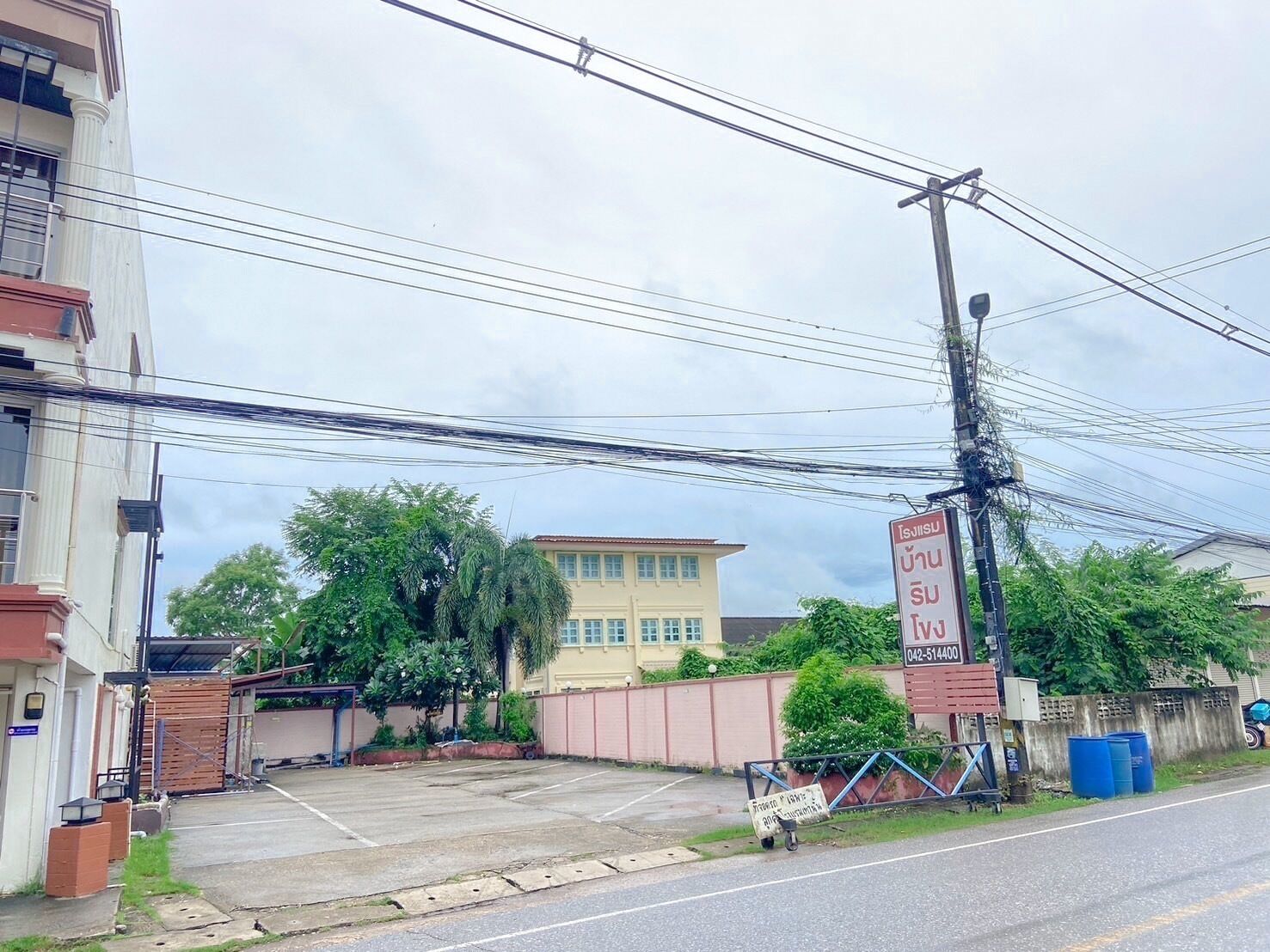 Ein Parkplatz mit befahrter Schranke, ein Gebäude mit gelber Fassade und ein Schild mit thailändischer Schrift.