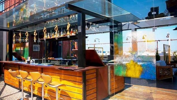 Een moderne bar met een houten toonbank en barstoelen, glazen scheidingswanden en uitzicht op de stadsgezicht.