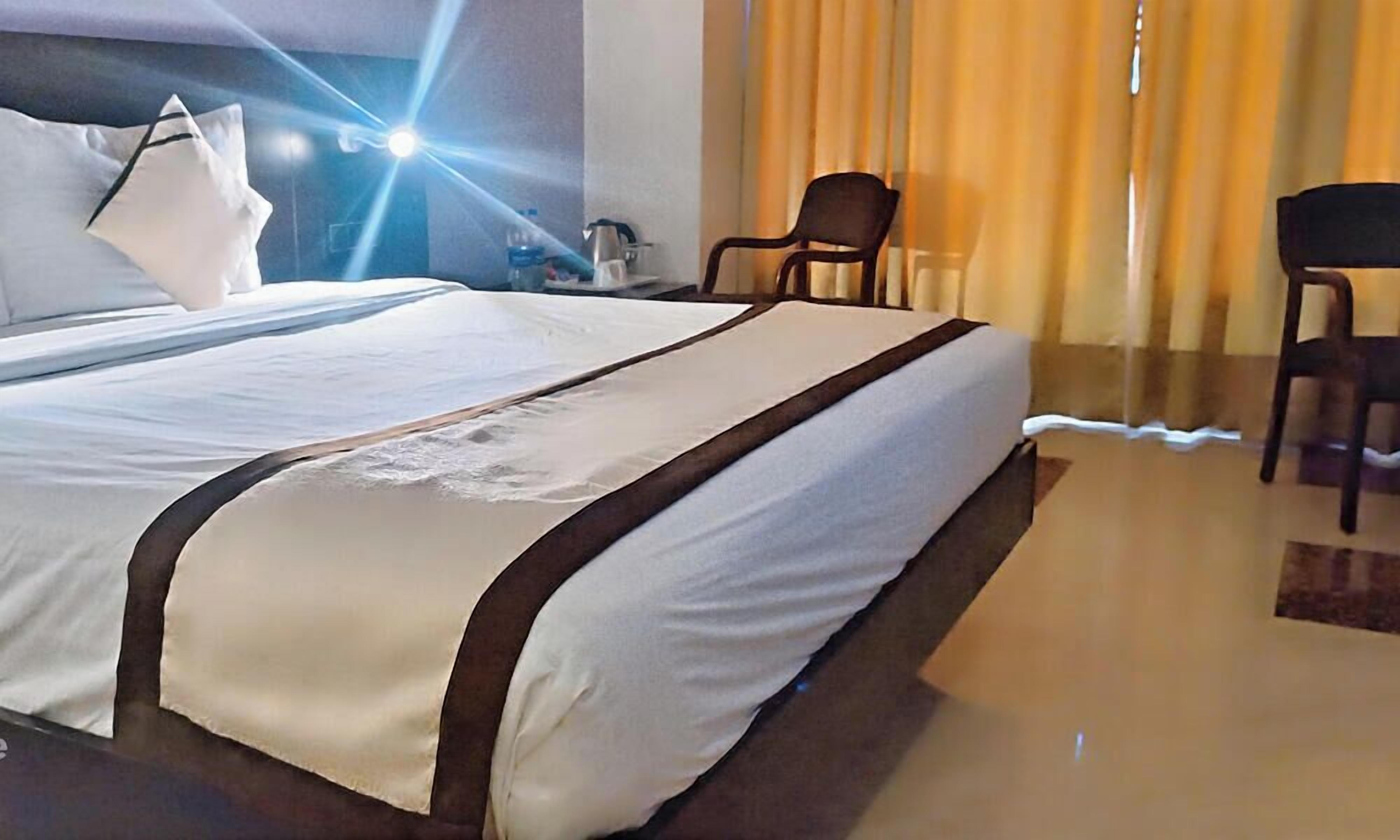 A hotel room with a large bed, two chairs, a nightstand, and a lamp.