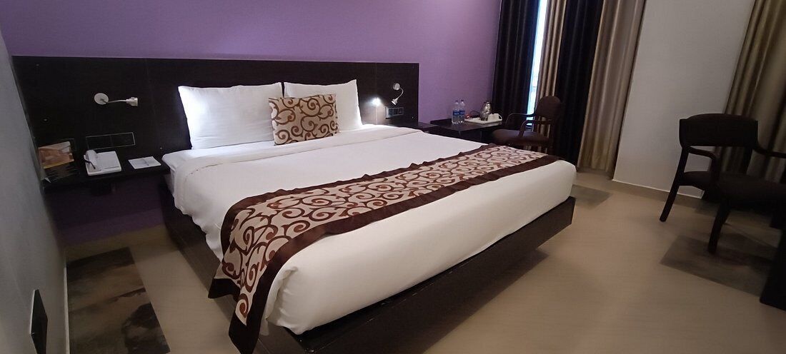 A hotel room with a large bed, a nightstand, a chair, and a desk with a lamp.