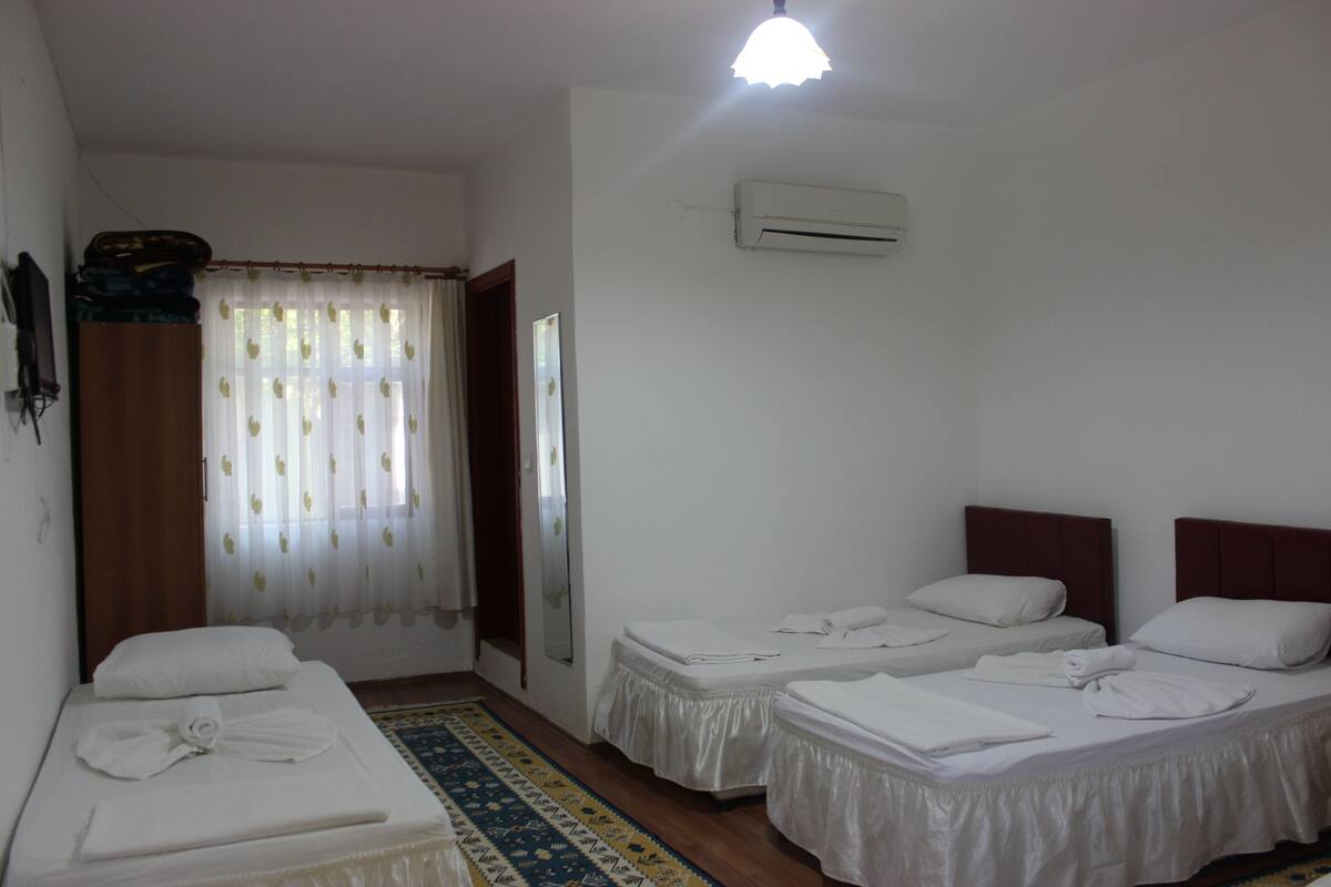 A hotel room with two single beds, a large mirror, an air conditioning unit, and a window with sheer curtains.