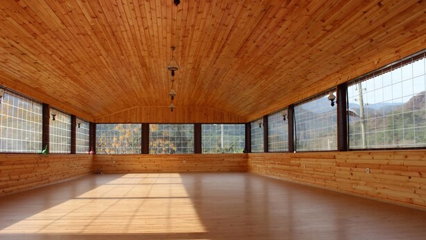 Ein geräumiges Zimmer mit Holzwänden und -decke, großen Fenstern und einem Holzboden.