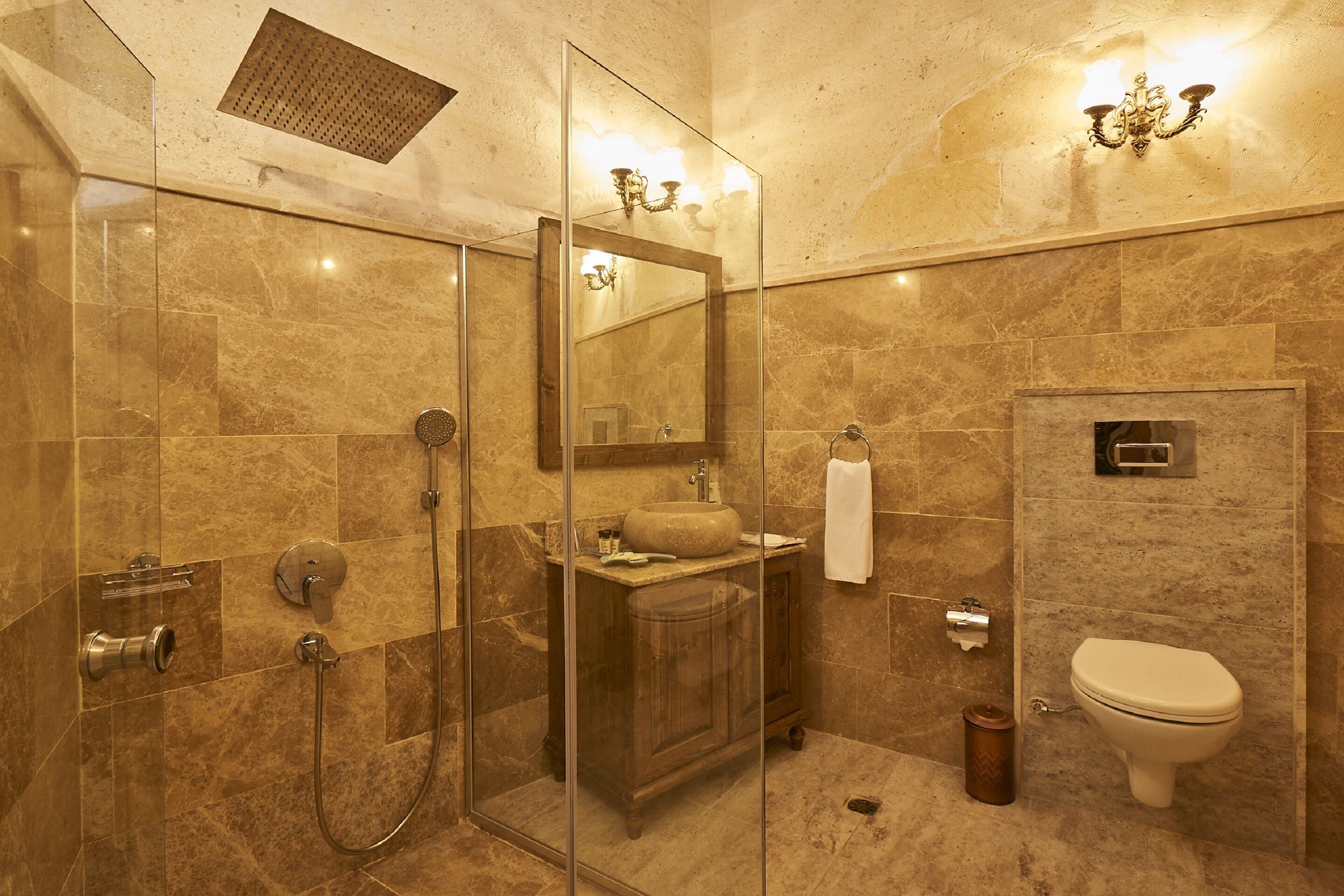 Un baño moderno con cabina de ducha de vidrio, tocador de madera, inodoro y pared con azulejos de mármol.