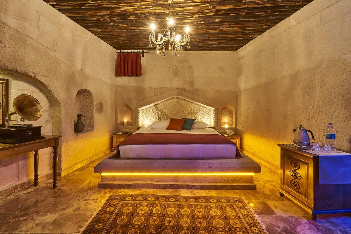 A bedroom with a large bed, a chandelier, a wooden table, and a nightstand.