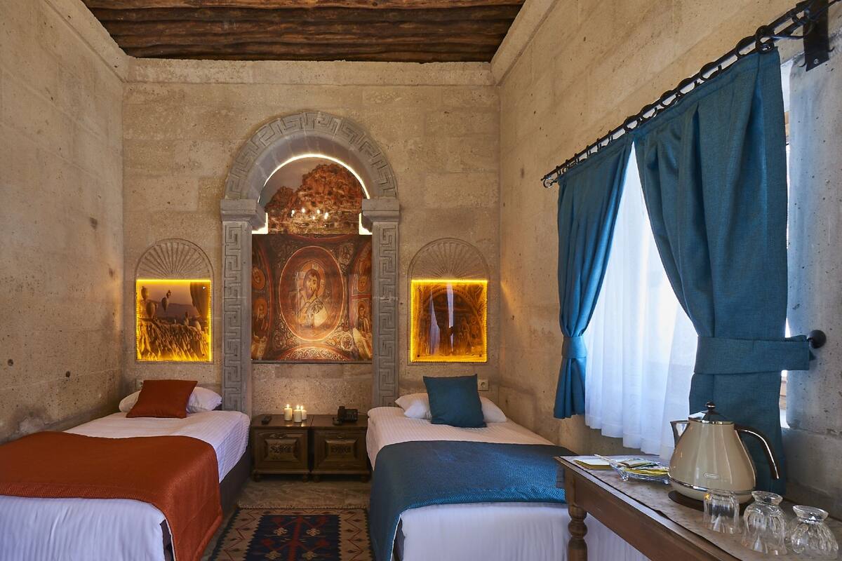 A room with two beds, a wooden table with a kettle, and a mural on the wall.