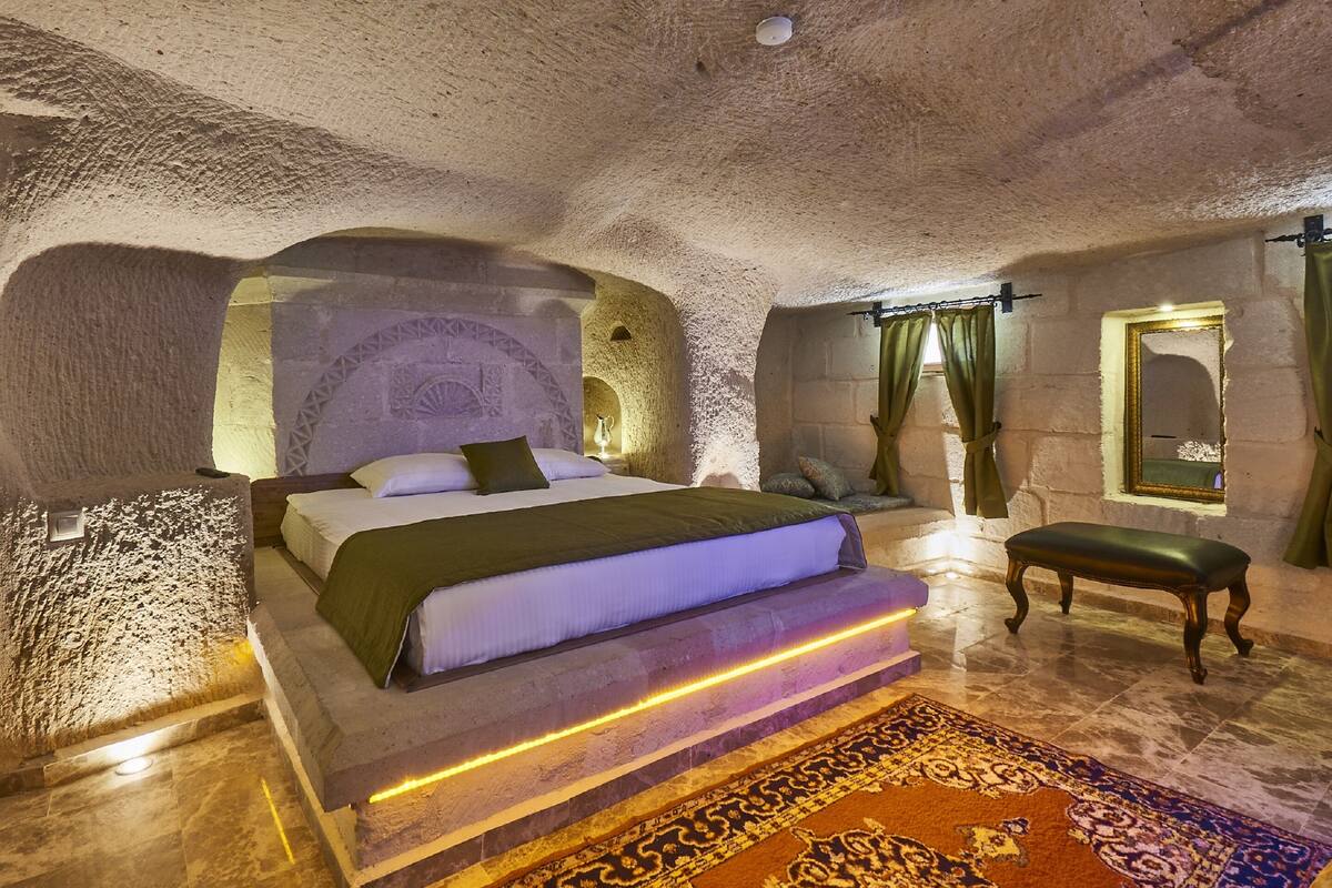 A bedroom with a stone ceiling, a bed with a green bedspread, a bench, and a patterned rug.