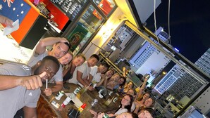 Un groupe de personnes est réuni dans un bar, avec une vue sur la ville en arrière-plan.