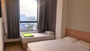 Une chambre à coucher avec un lit, une fenêtre avec des rideaux et une vue sur les bâtiments à l’extérieur.