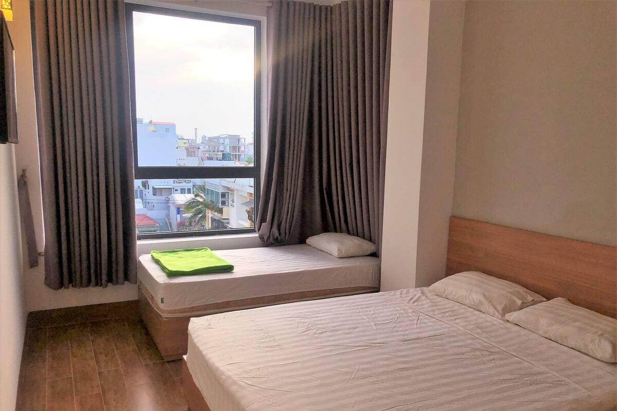 Een slaapkamer met een bed, een raam met gordijnen en een uitzicht op gebouwen.
