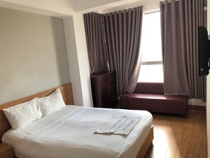 Hotelkamer met een bed, houten hoofdbord, een houten dressoir, een bankje en een raam met gordijnen.