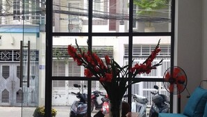 Une pièce avec une grande fenêtre, un ordinateur portable posé sur une table en bois, un vase rempli de fleurs rouges et un canapé bleu.
