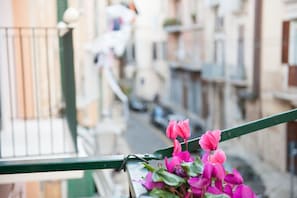 A balcony with a railing, pink flowers, and a narrow street in the background. - B&B Bari Old Town (Bari)