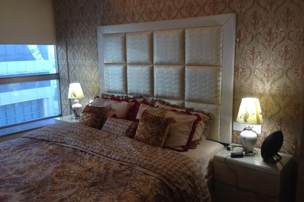A bedroom with a large bed, two bedside lamps, a nightstand, and a window with a view.