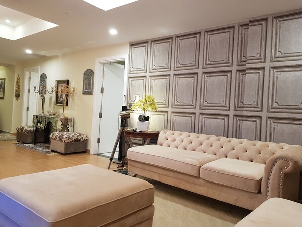 A spacious living room with a large beige sofa, matching ottoman, and a decorative wall paneling.