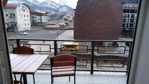 Ein Balkon mit Tisch und Stühlen, Blick auf einen gelben Bus und Gebäude im Hintergrund.