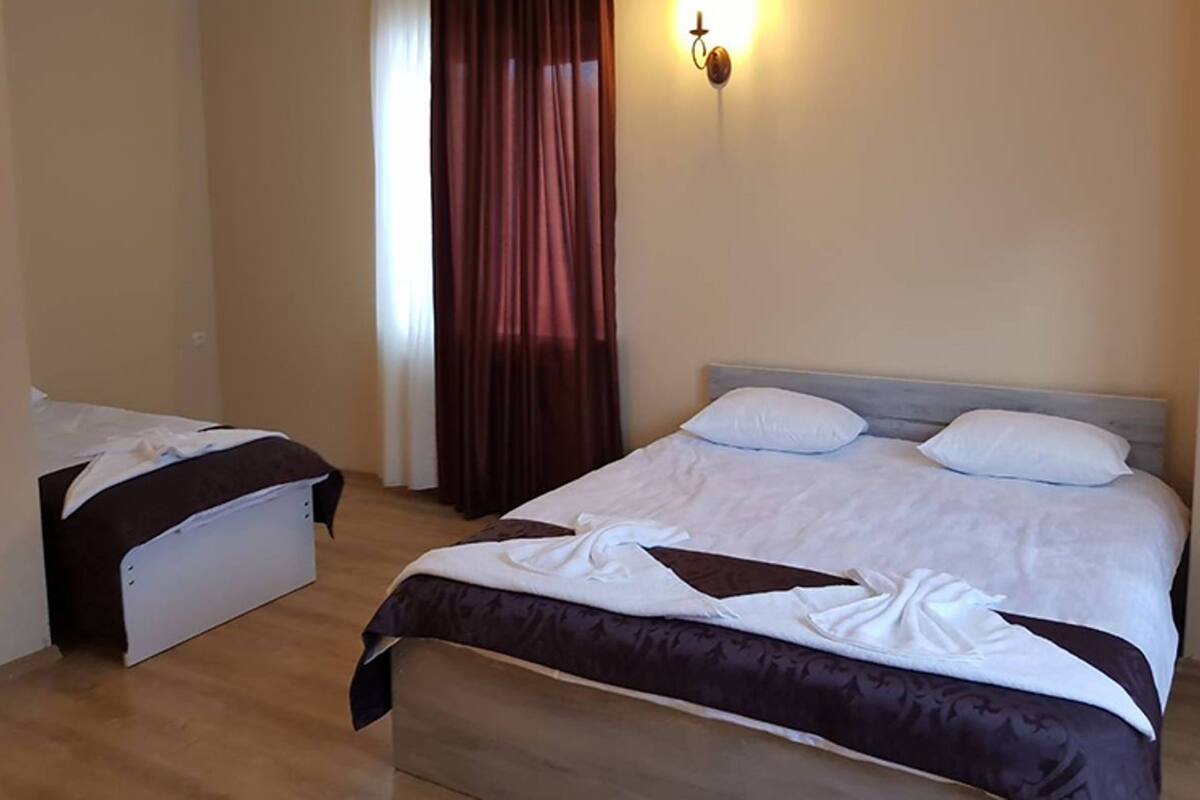Une chambre d’hôtel avec deux lits, un plancher en bois, un luminaire fixé au mur et une fenêtre avec des rideaux.