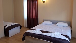 Ein Hotelzimmer mit zwei Betten, Holzboden, einer Wandleuchte und einem Fenster mit Vorhängen.