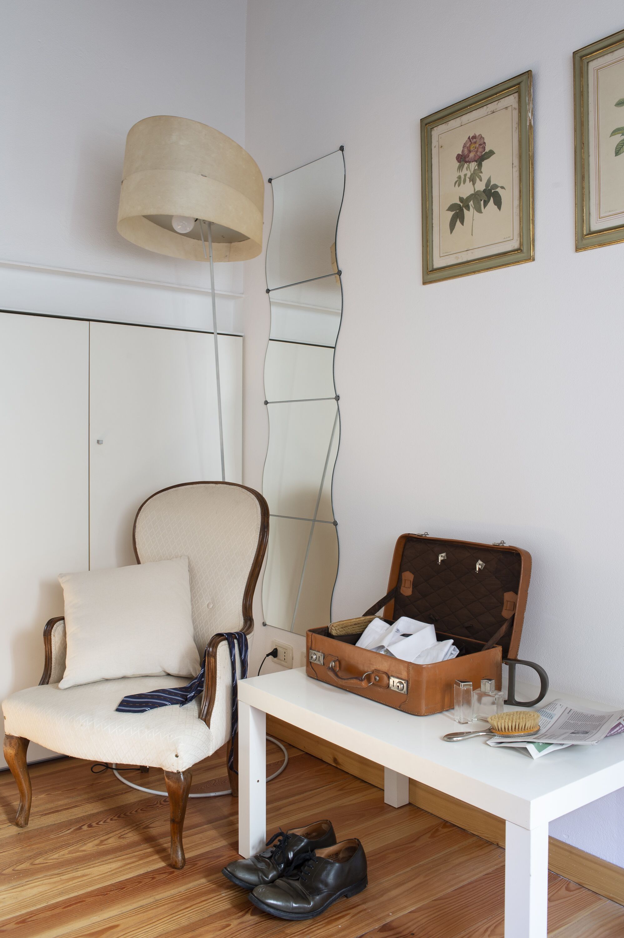 A room with a white chair, a bench, a suitcase, and a lamp.