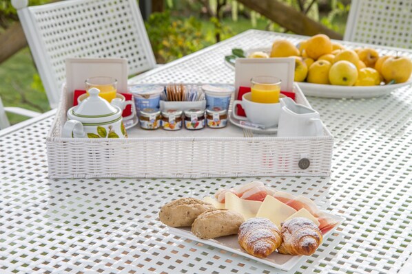 A breakfast setup with pastries, fruits, and beverages on a white wicker table outdoors.