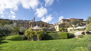 A traditional stone building with a garden in front, surrounded by other stone buildings. - B&B Porta Castellana (Montalcino)