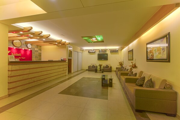 A hotel lobby with a reception desk, sofas, a coffee table, and a clock on the wall.