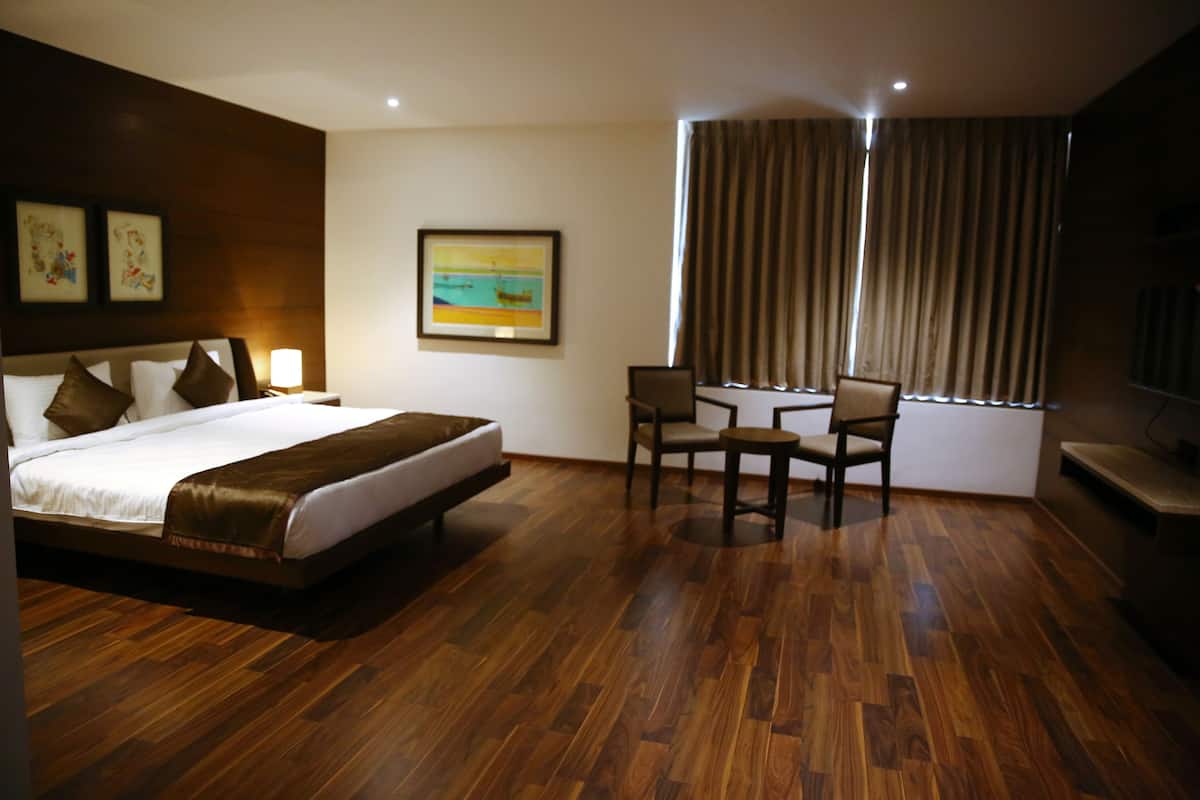 A hotel room with a large bed, a small table with two chairs, a TV, and a painting on the wall.