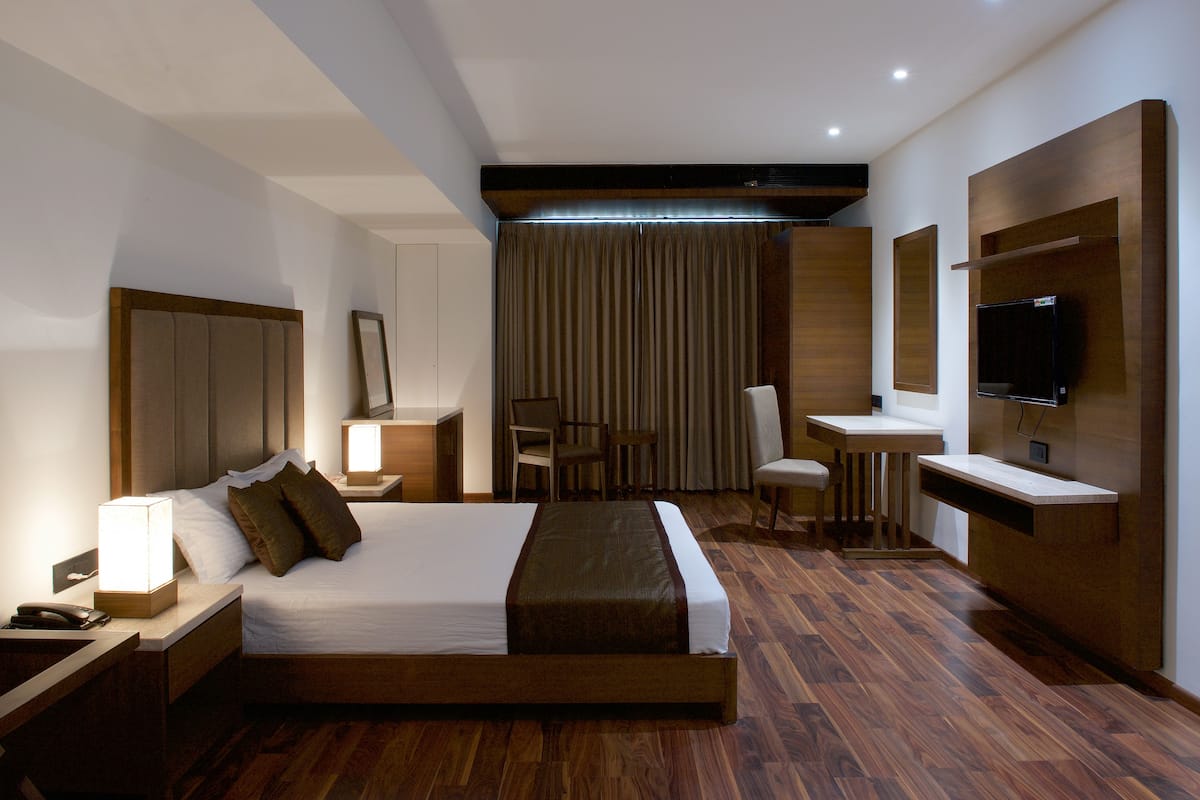 A hotel room with a large bed, bedside tables, a desk, a chair, a television, and a curtain.